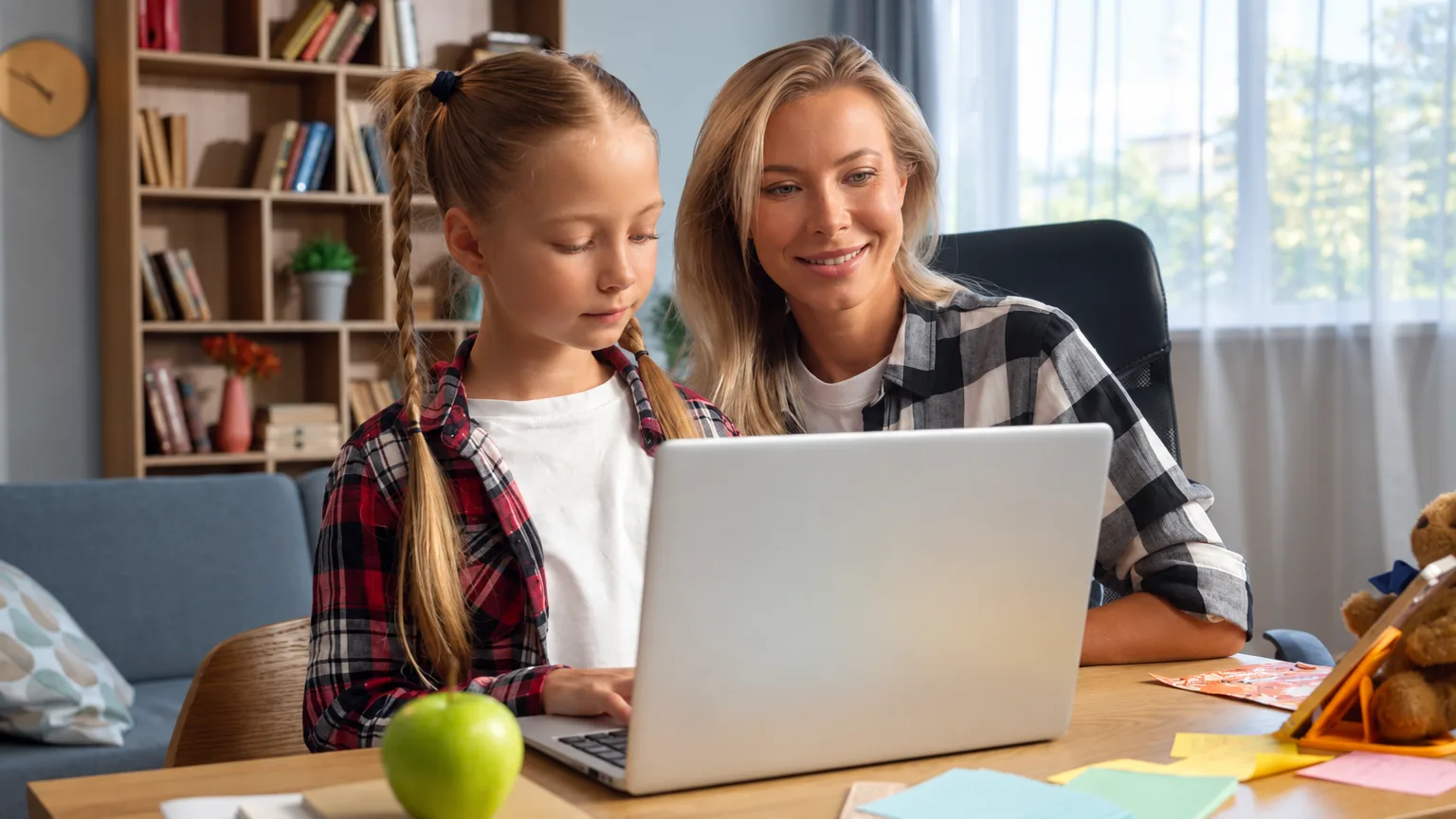 A mother helping her daughter with homework at a laptop